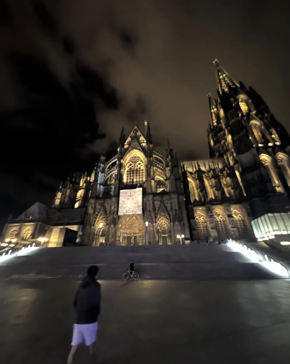 Cologne Cathedral lit up at night under heavy clouds