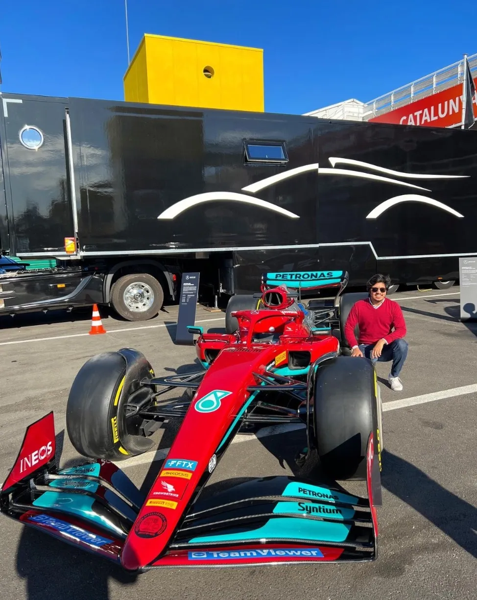 Hassan crouching next to a Mercedes Formula 1 show car